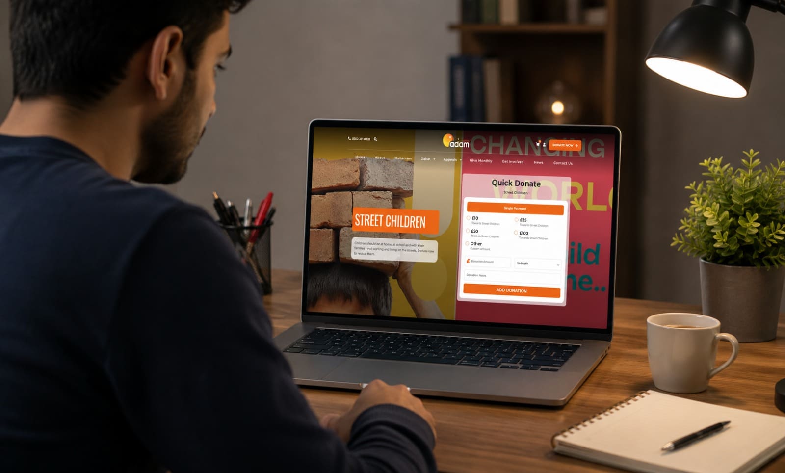 A man looking at a laptop screen displaying an online donation page for street children, featuring a "Quick Donate" form on a wooden desk with a lamp, coffee mug, and notebook.